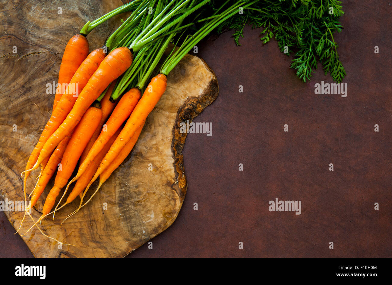 Mazzetto di crudo fresco carote arancione con foglie verdi bush sul tagliere di legno Foto Stock