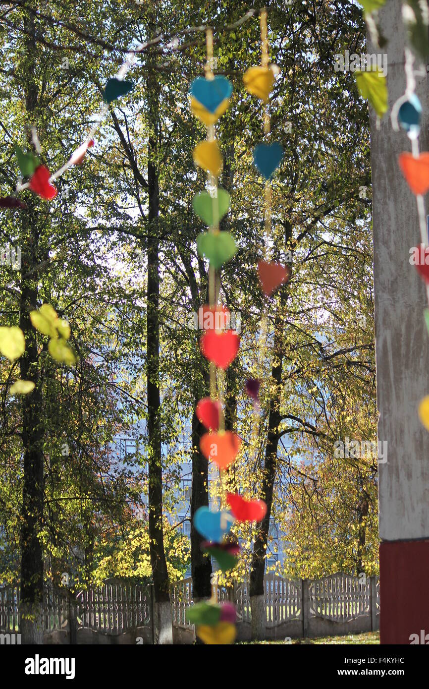 Luminose colorate Cuori di carta su nastro appendere su albero in posizione di parcheggio Foto Stock
