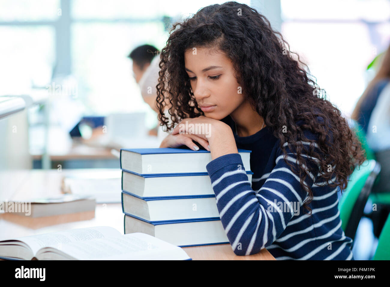 Giovani curly African American Girl è seduto in un umore triste mettendo la sua testa sui libri Foto Stock