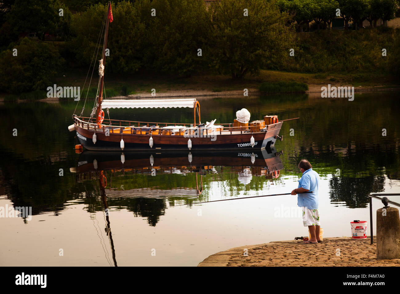 Un uomo pesca al Quai Salvette in Bergerac Francia davanti a un ormeggiata la barca turistica Foto Stock