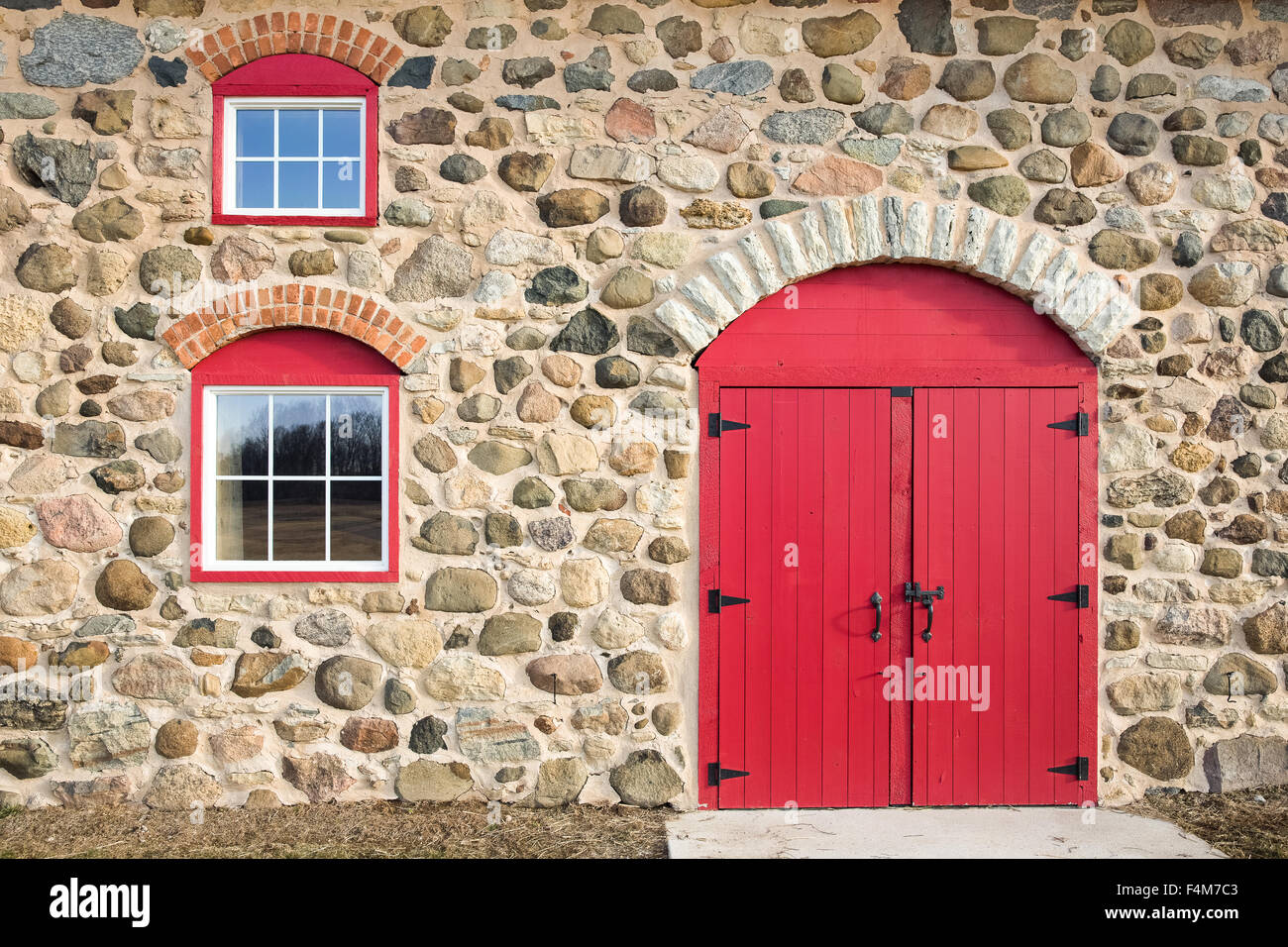 Rosso brillante porta ad arco e due finestre impostato in un campo vecchio muro di pietra. Un sacco di consistenza, colore e artigianato. Foto Stock