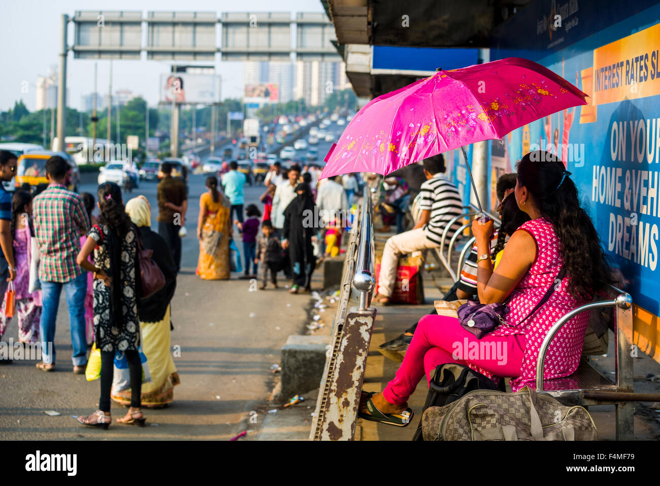 Le persone sono in attesa di un bus del sistema dei trasporti pubblici presso l'autostrada, una donna è utilizzando un ombrello rosa per ombra Foto Stock