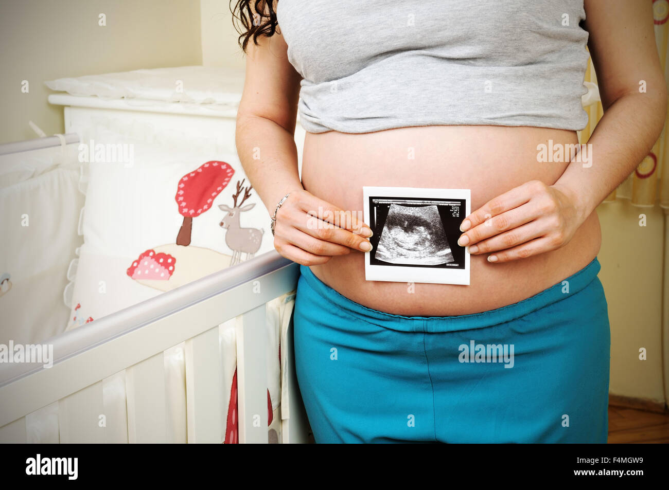 Ritagliato closeup di una gestante in possesso di una immagine ad ultrasuoni su di lei baby bump Foto Stock