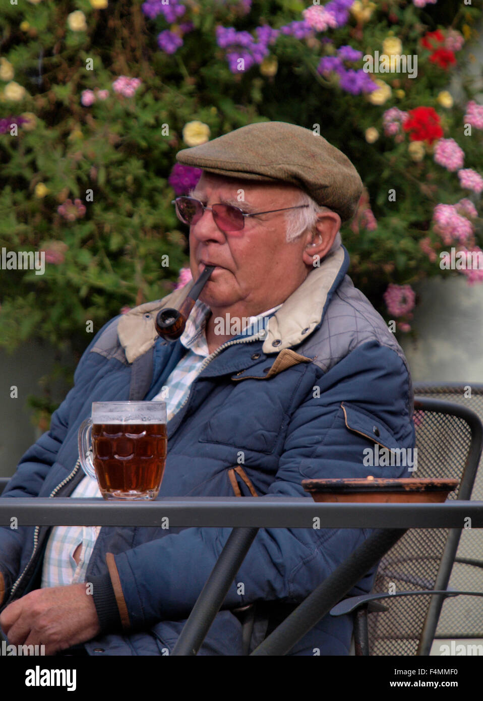 Il vecchio uomo seduto fuori da un pub con una pinta di birra e il tubo, Cornwall, Regno Unito Foto Stock