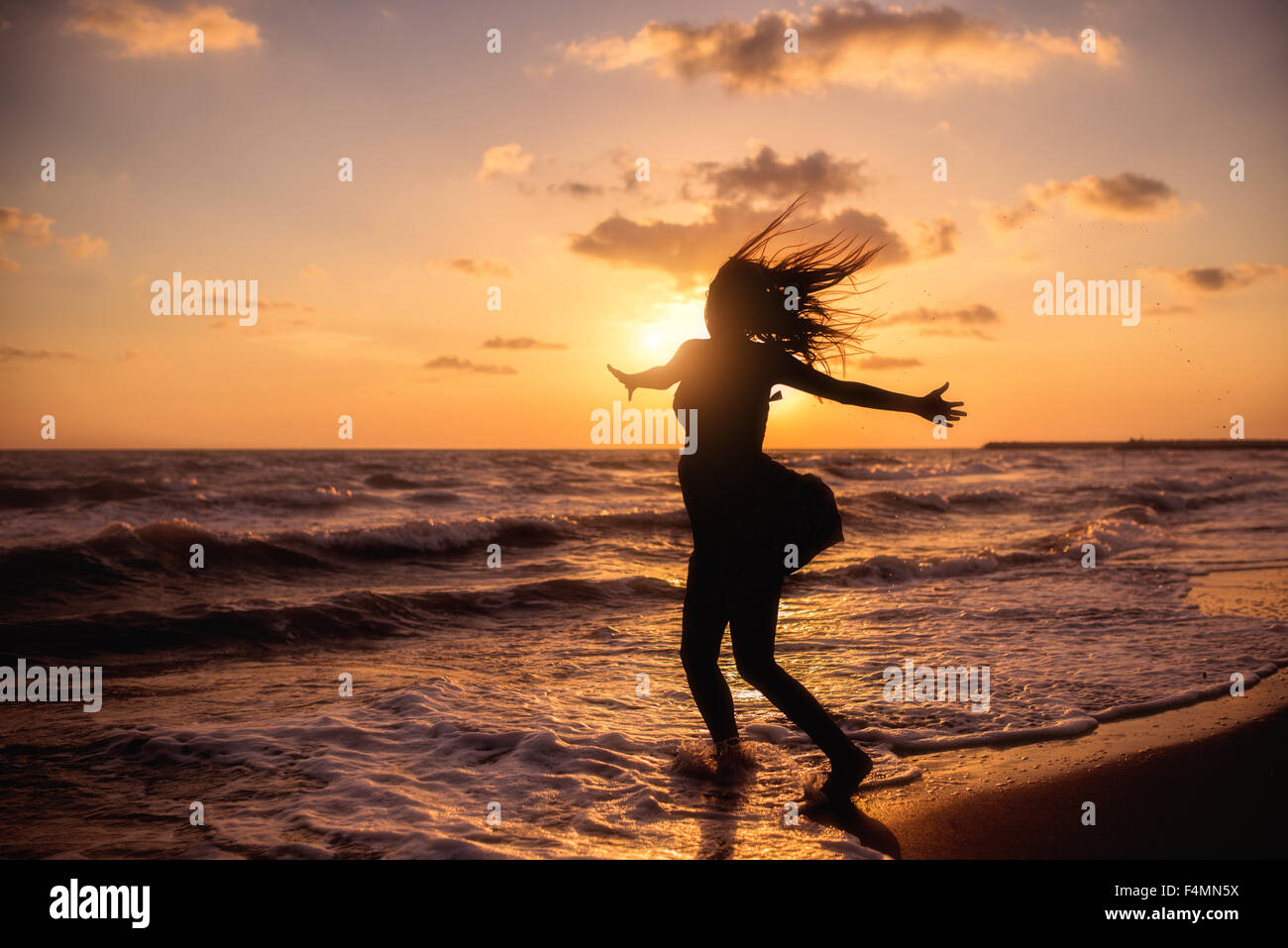 Donna felice il salto nel tramonto sul mare Foto Stock