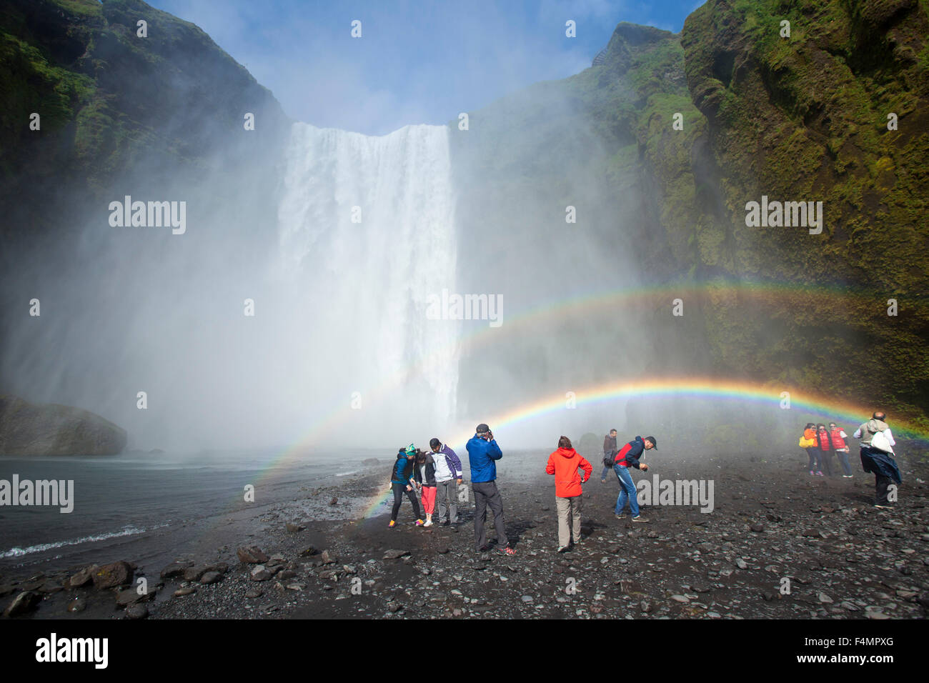 I turisti al rainbow al di sotto di 60m-alta cascata Skogafoss, Skogar, Sudhurland, Islanda. Foto Stock