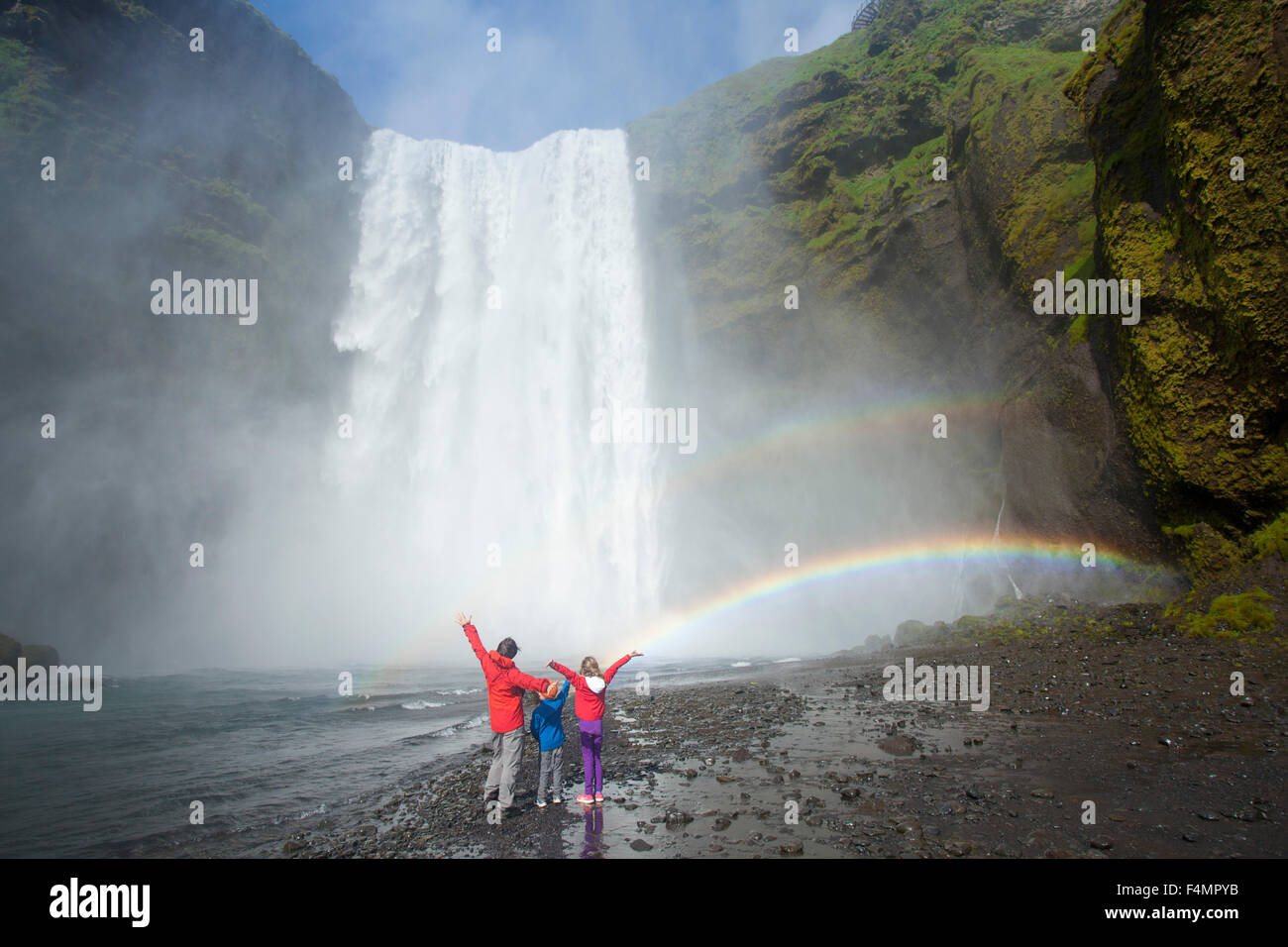 La famiglia in rainbow sotto 60m-alta cascata Skogafoss, Skogar, Sudhurland, Islanda. Foto Stock