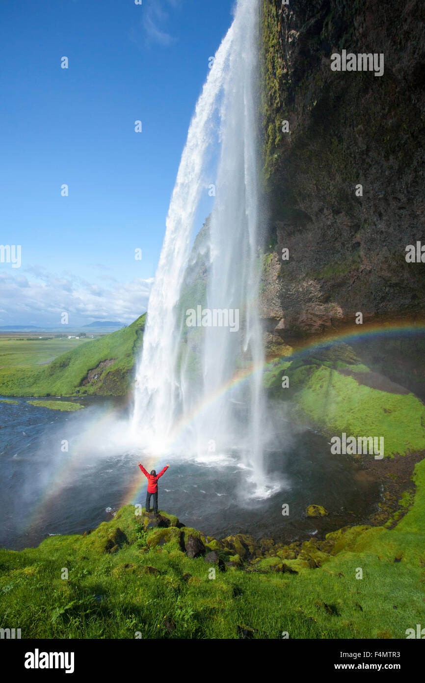 Persona e rainbow sotto 60m-alta cascata Seljalandsfoss, Sudhurland, Islanda. Foto Stock