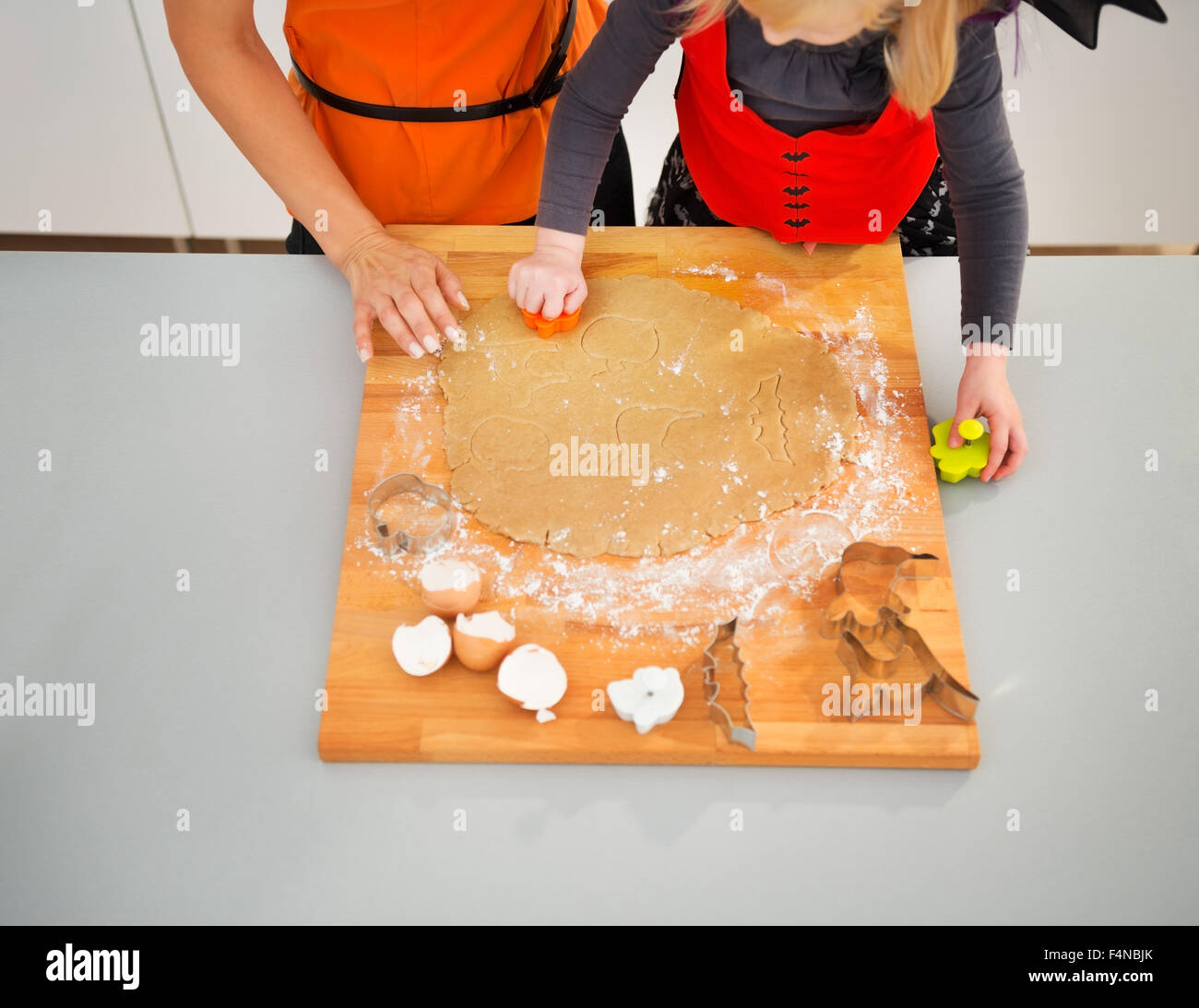 Primo piano su halloween vestito della bambina con la madre facendo biscotti freschi di pasta arrotolata in cucina. Tradizionale autunno holiday Foto Stock