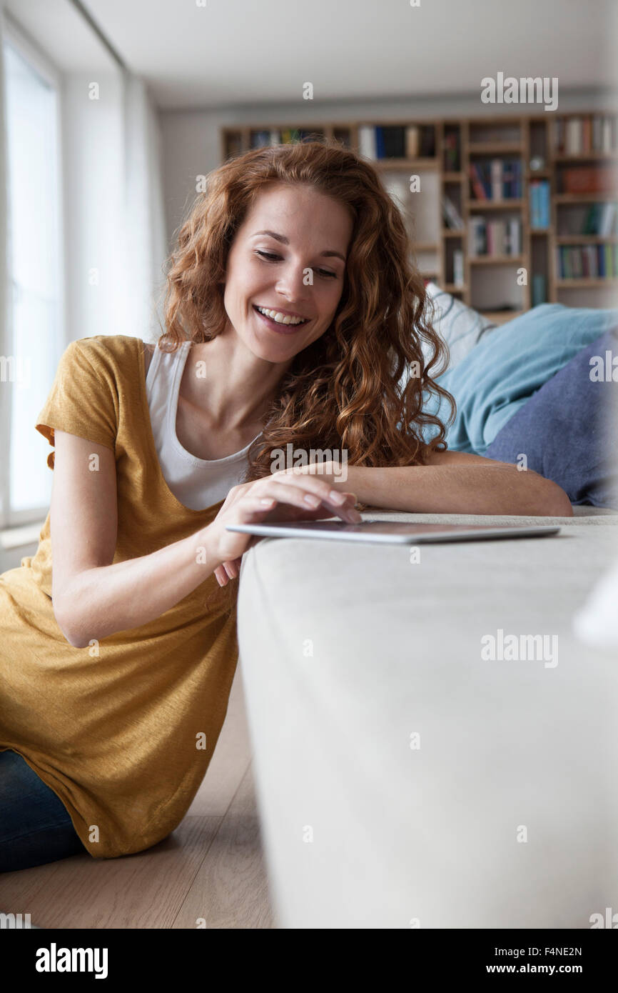 Donna sorridente a casa utilizzando la tavoletta digitale sul lettino Foto Stock