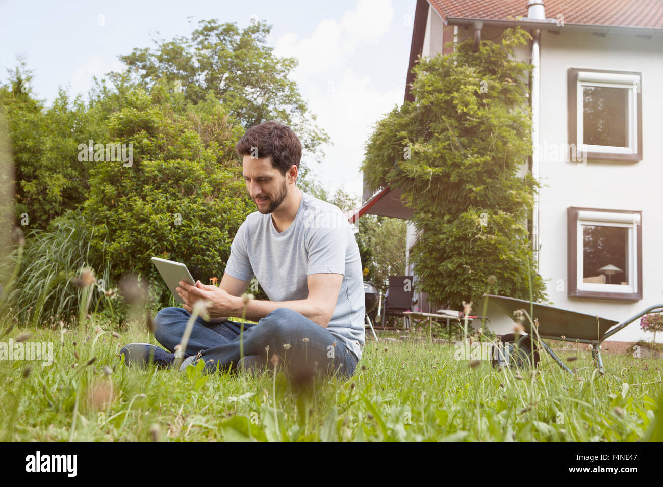 Uomo seduto in giardino con tavoletta digitale Foto Stock