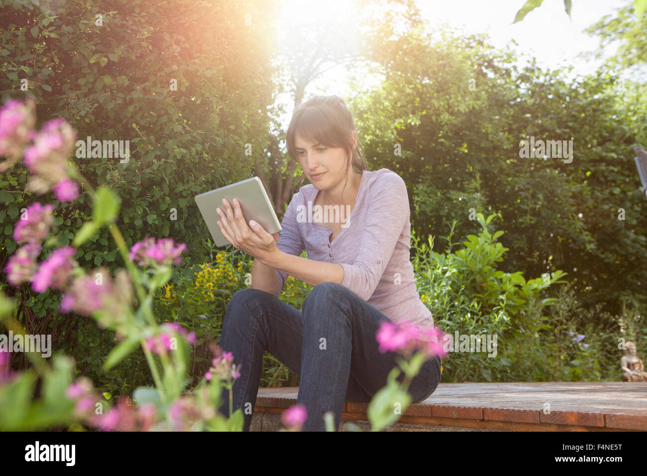 Donna seduta in giardino con tavoletta digitale Foto Stock