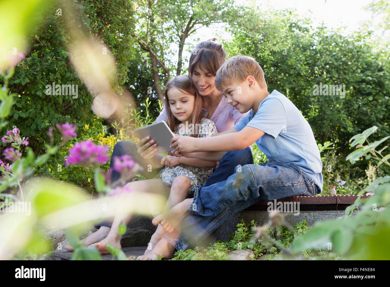 Madre e figlio e figlia con tavoletta digitale in giardino Foto Stock