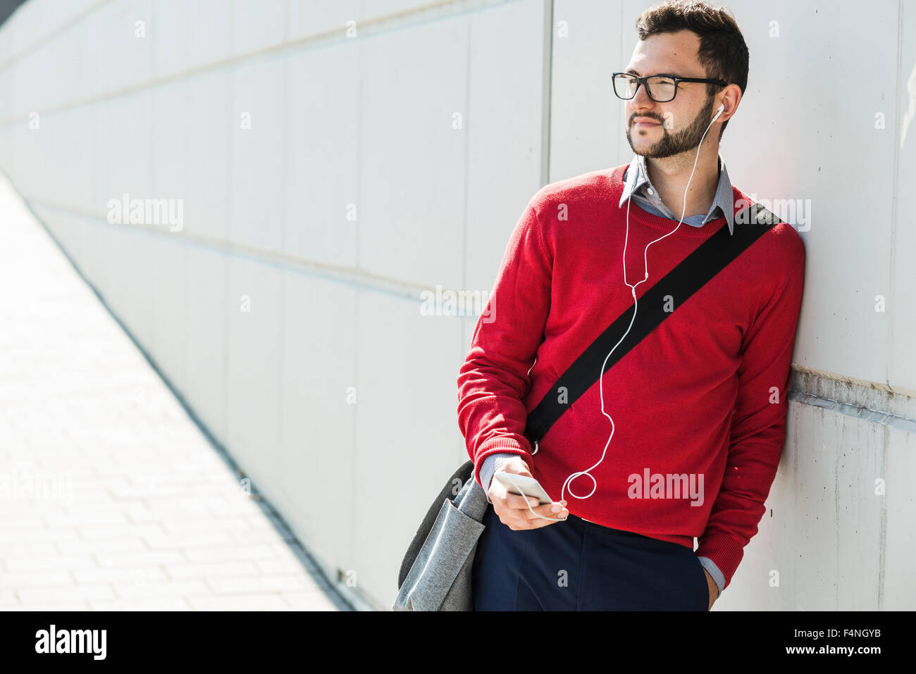 Giovane imprenditore utilizzando smart phone, indossa auricolari Foto Stock