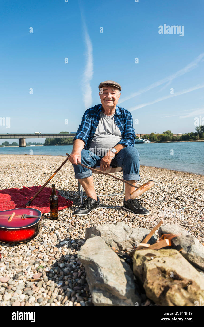 Germania, Ludwigshafen, ritratto di sorridere senior uomo salsiccia barbecueing sulla spiaggia Foto Stock