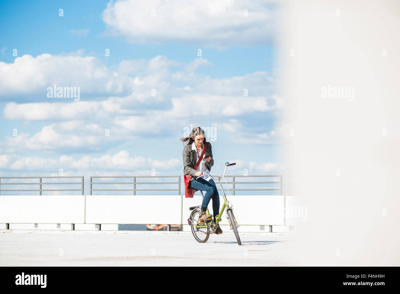 Giovane donna in bicicletta guardando al telefono cellulare Foto Stock