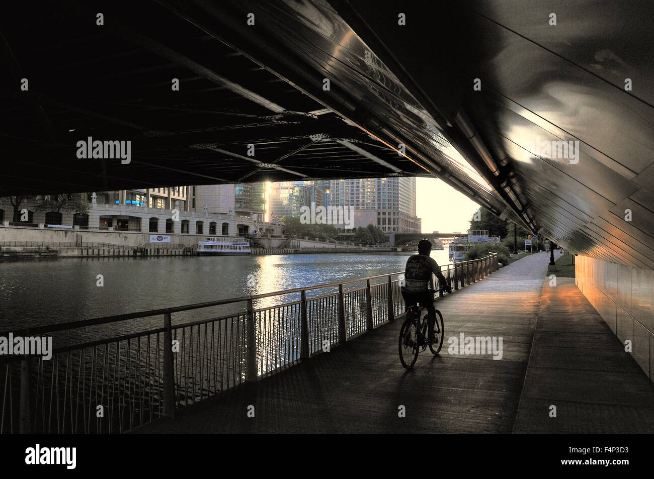 Un ciclista pedala sul lungofiume sotto Chicago's Michigan Avenue ponte verso il sorgere del sole su un inizio di mattina d'estate. Chicago, Illinois, Stati Uniti d'America. Foto Stock