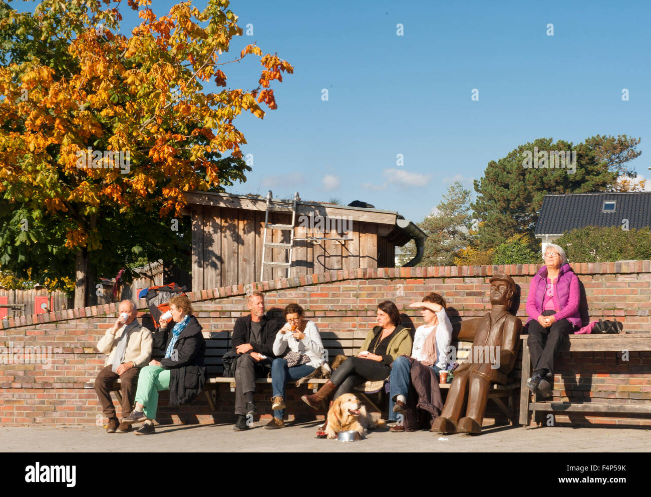 Le persone che si godono il sole autunnale su un banco di lavoro accanto al porto di kiosk Niendorf / Ostsee, un porto di pesca nel Mar Baltico Foto Stock