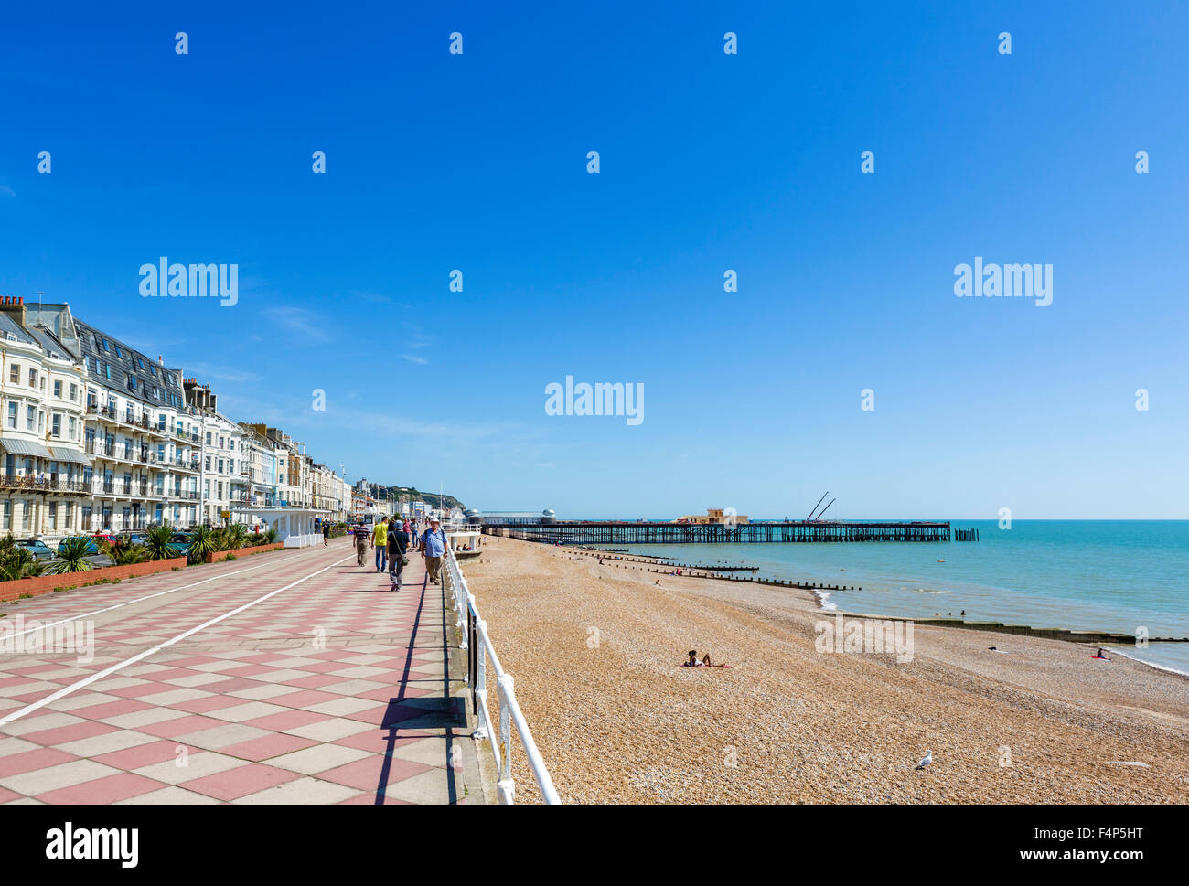 Il lungomare e la spiaggia con la bruciata pier nella distanza, Hastings, East Sussex, England, Regno Unito Foto Stock