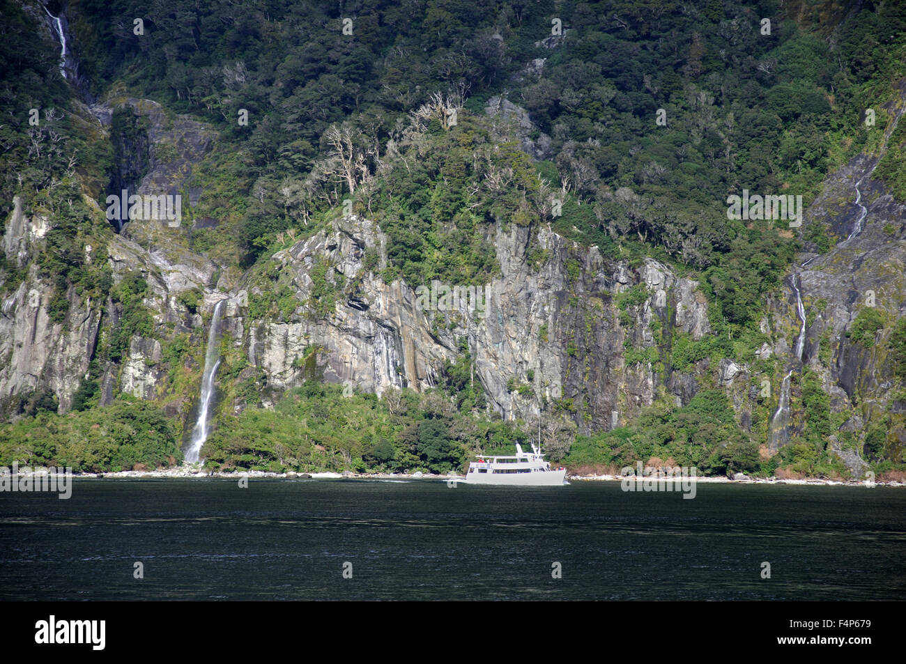 Lancio turistico passa un ONU-denominato Waterfall a Milford Sound, Fiordland, Nuova Zelanda Foto Stock