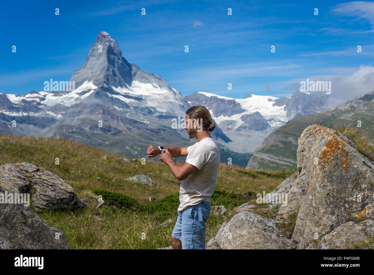 Trekker controlla il suo smartwatch sotto il famoso Cervino picco. Luglio, 2105. Il Cervino, Svizzera. Foto Stock