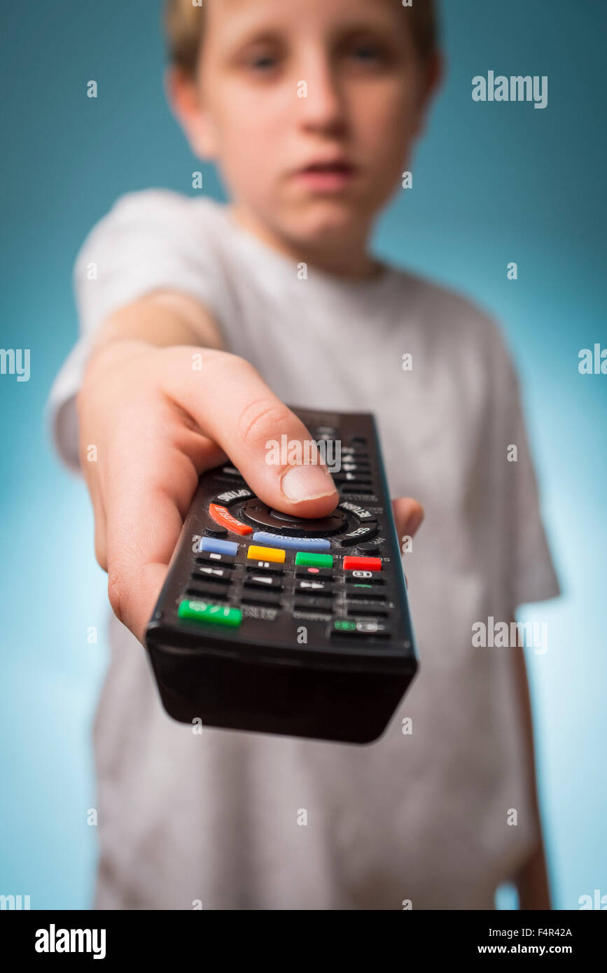 Un annoiato ragazzo cambiando canali utilizzando un telecomando del televisore Foto Stock