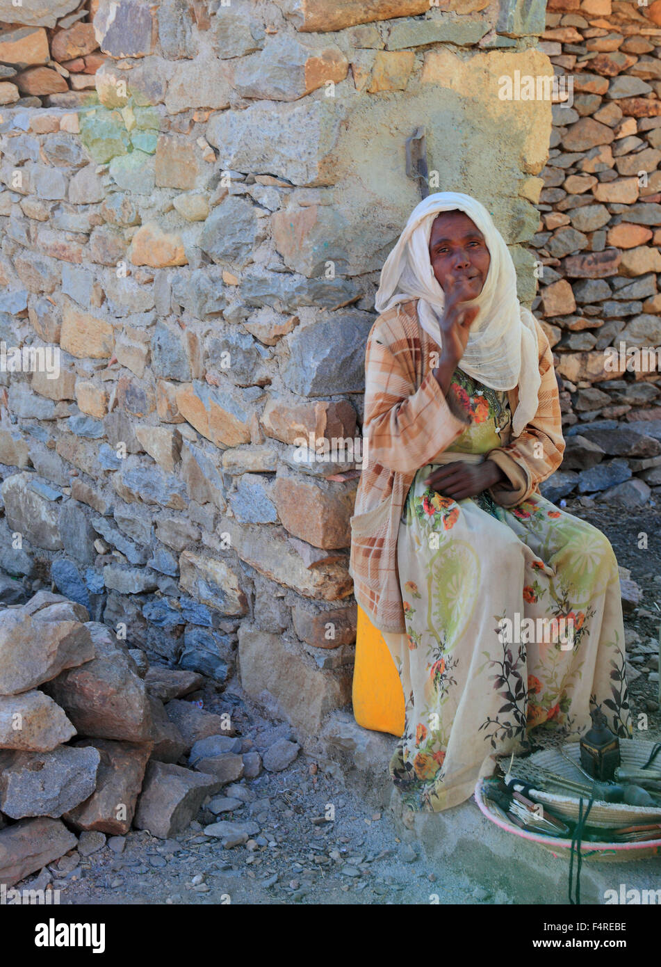 Donna in abito nativo, seduto contro un muro e vende souvenir Foto Stock