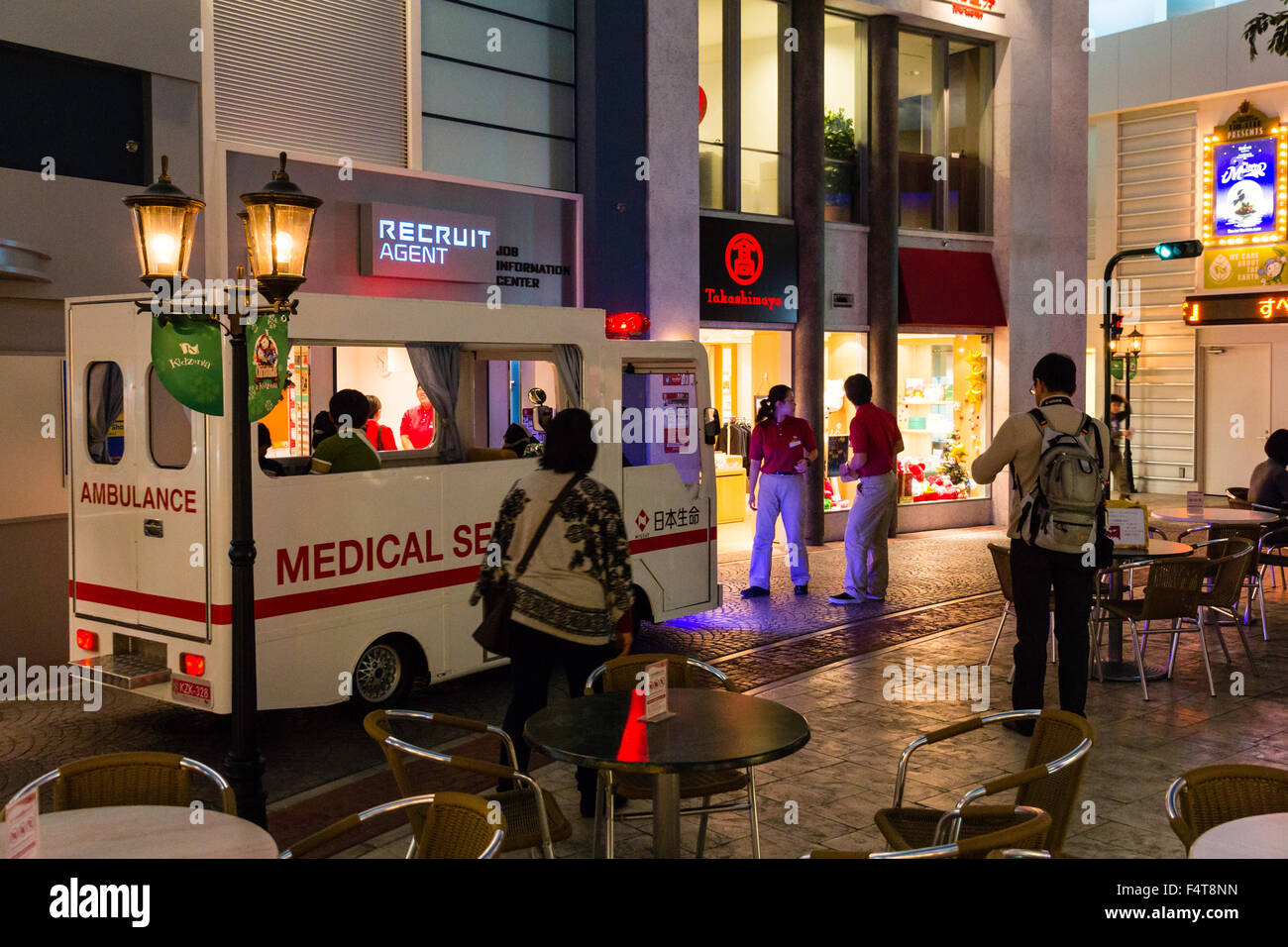 Giappone, Nishinomiya, KidZania, bambini gioco di ruolo dei centri di attività. Studio street e bambini guida ambulanza lungo passato edifici, di notte. Foto Stock