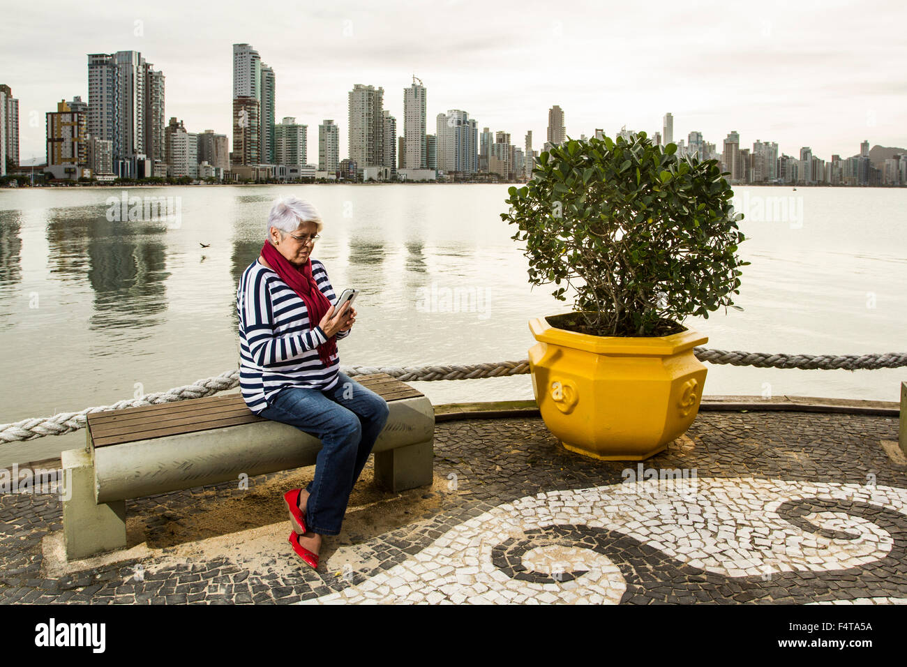 Donna anziana sul telefono cellulare seduta su una panchina a Pontal da Barra Sul. Balneario Camboriu, Santa Catarina, Brasile. Foto Stock