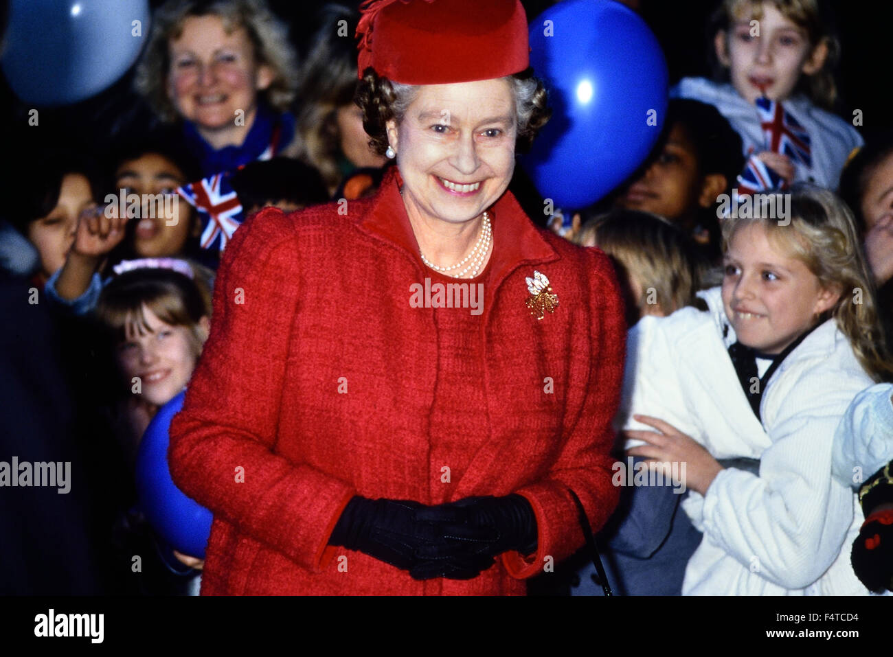Un sorridente HRH Queen Elizabeth II per una visita reale al Queen Mary College circondato da felice ed emozionato i bambini Foto Stock
