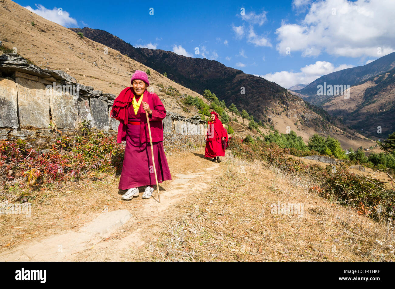 I monaci e le monache di indossare i panni di colore rosso a piedi su un piccolo sentiero lungo un pendio di montagna Foto Stock