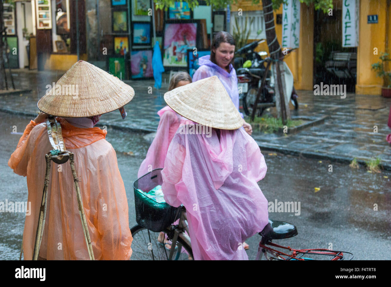 Due donne vietnamita e un turista occidentale indossando i Mac in plastica in Hoi An vietnam durante una tempesta di pioggia. Foto Stock