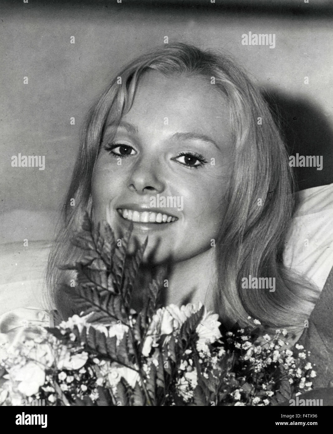 Una bionda modello con capelli lunghi sorridente dietro un mazzo di fiori Foto Stock