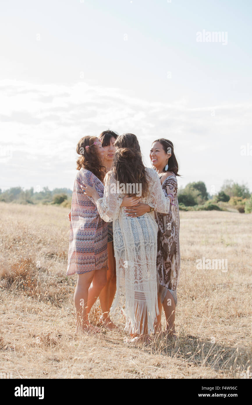 Boho donne abbracciando in un cerchio nel soleggiato campo rurale Foto Stock