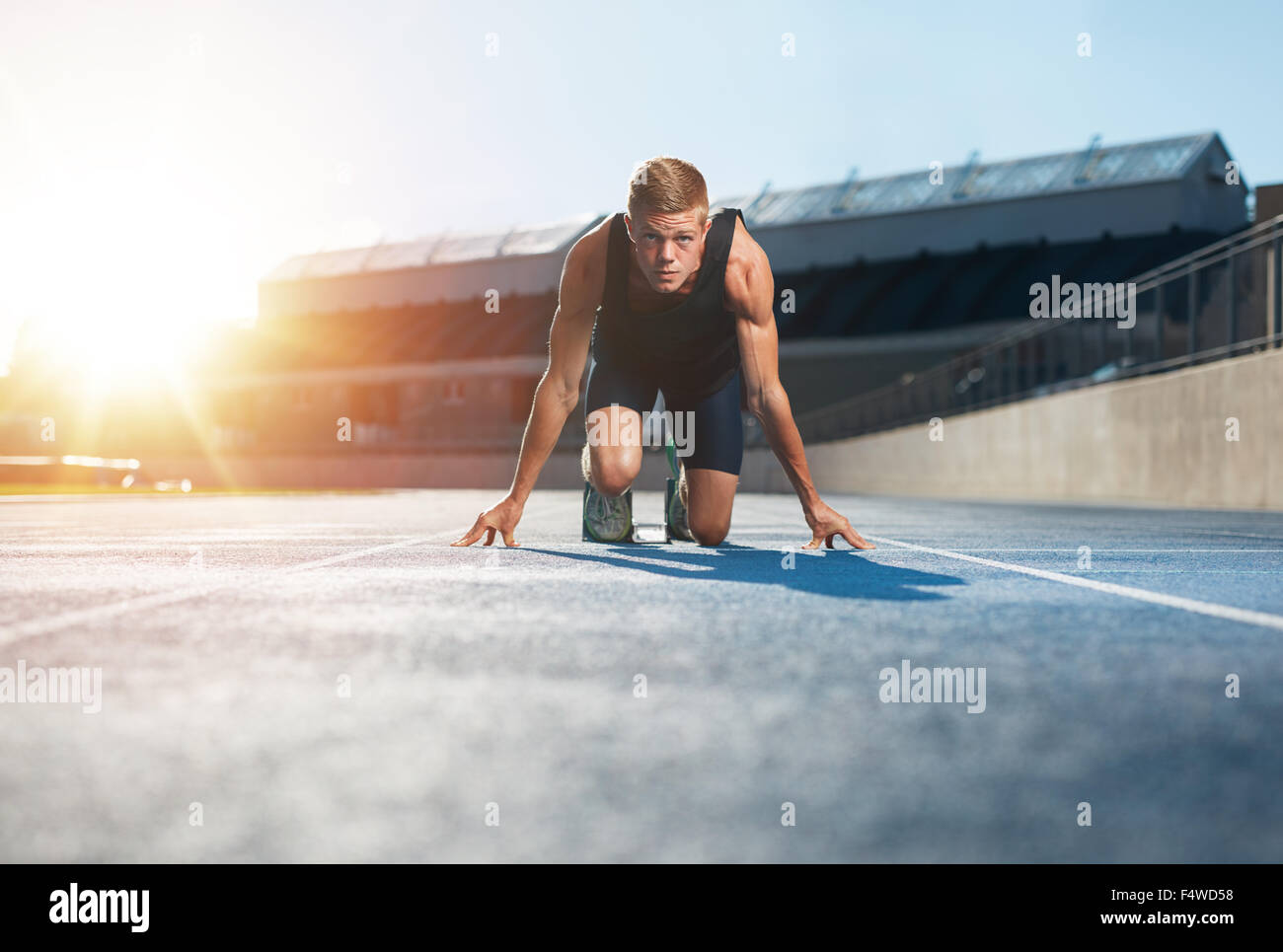 Il giovane atleta nella posizione di partenza pronta per iniziare una corsa. Velocista maschio pronto per una corsa su pista guardando con fotocamera Foto Stock
