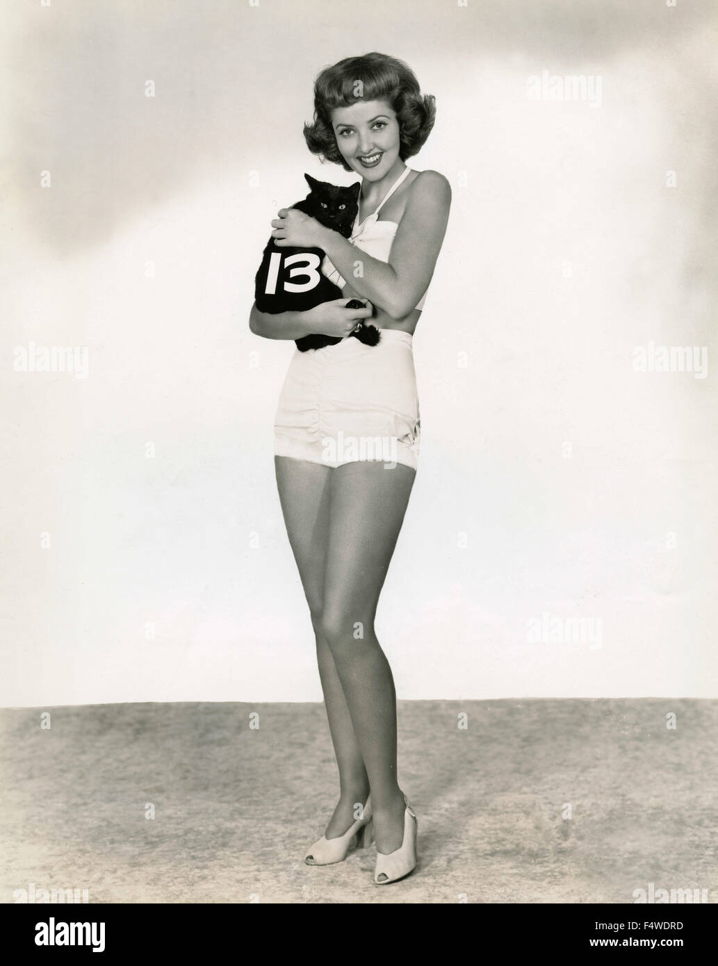 L'attrice americana Martha Vickers in un costume da bagno ​​white tenendo un gatto nero con il numero 13 Foto Stock