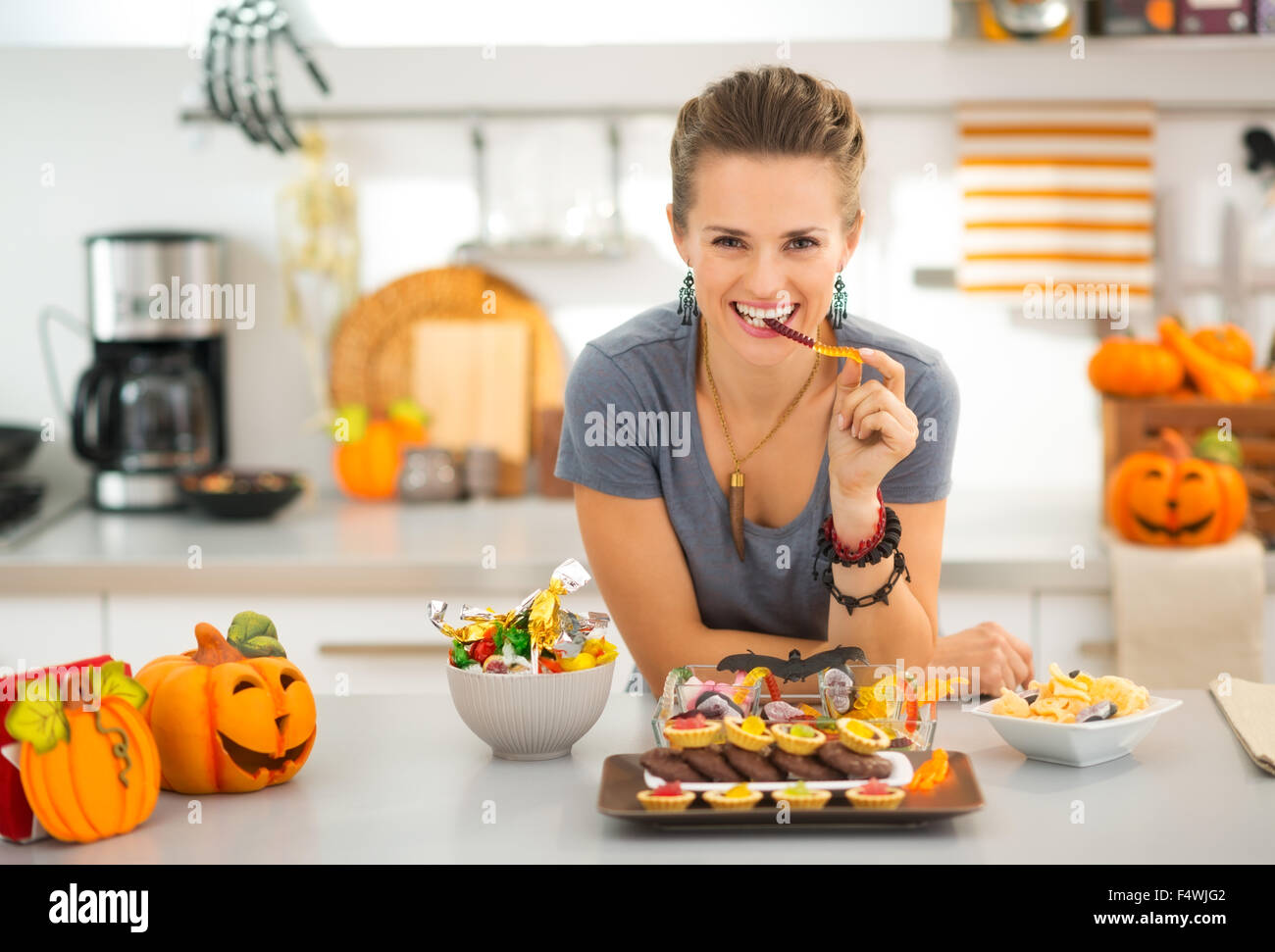 Pronto per la Festa di halloween! Donna sorridente in cucina decorata mangiare halloween Trick or Treat candy, in attesa poco briganti invasione. Tradizionale autunno vacanza. Foto Stock