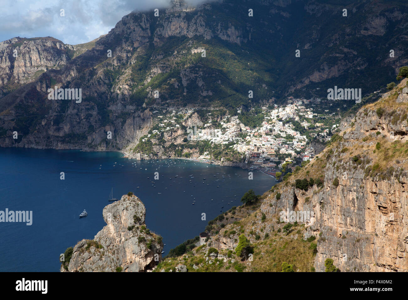 Vista in lontananza Positano, Costiera Amalfitana, con il mare e le barche e le rocce in primo piano Foto Stock