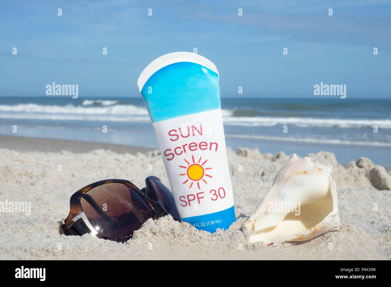 Bottiglia di sunscreen con shell e occhiali da sole sulla spiaggia. Foto Stock