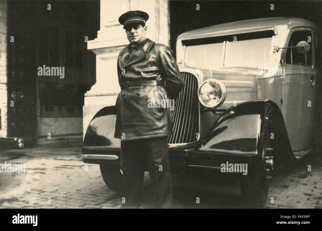 Driver con cappello e il cappotto di pelle accanto a una berlina, Italia Foto Stock