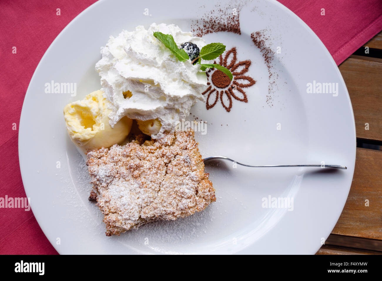 Piastra bianca di apple crumble dessert con gelato e cioccolato in polvere con una forcella su un tavolo di legno al top con una tovaglia rossa Foto Stock