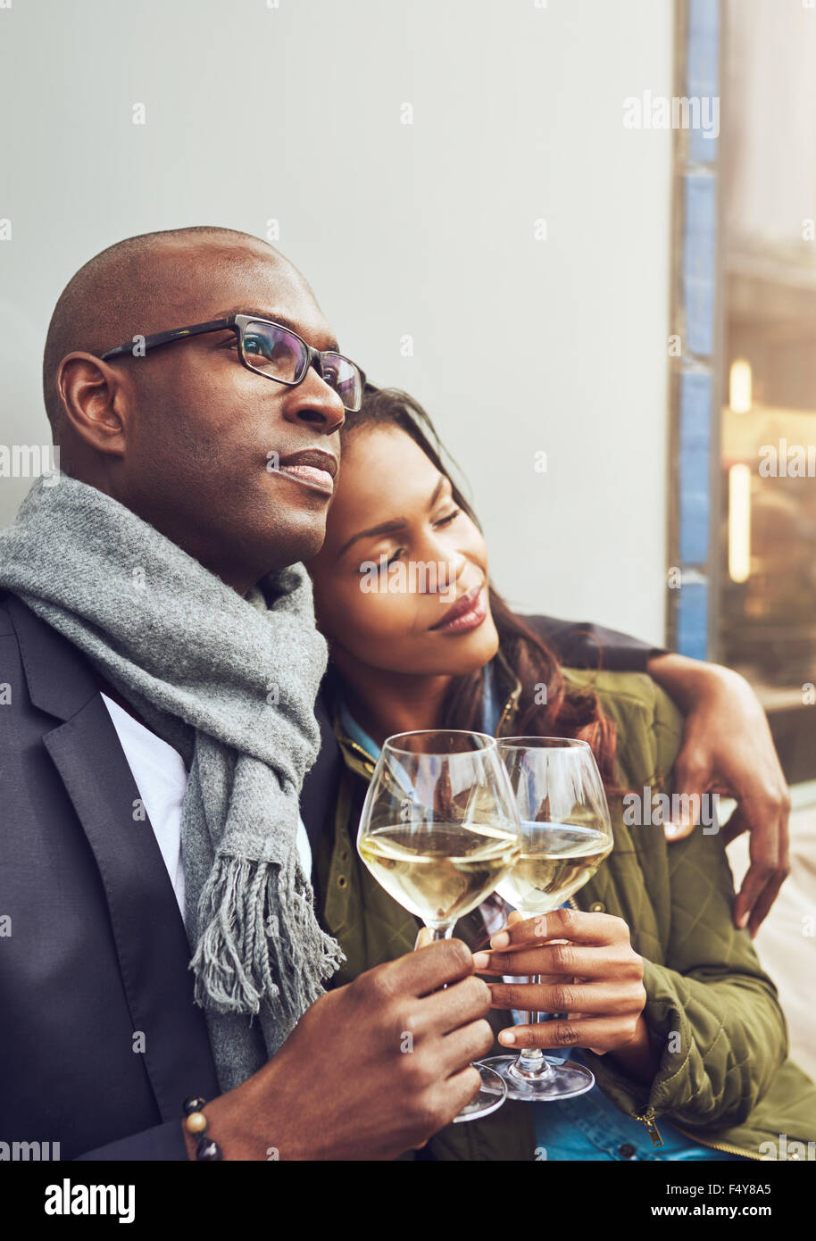 Amorevole coppia africana di godere di un momento di gara rilassante in un abbraccio in ogni altri braccia su bicchieri di vino bianco freddo Foto Stock