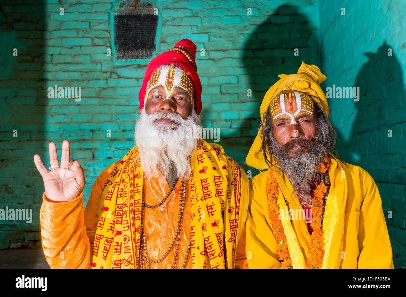 2 giallo vestito sadhus, uomini santi, che pongono di fronte a un muro verde Foto Stock