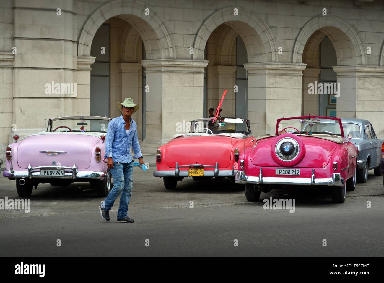Città cubane cowboy attraversando a piedi il plaza con parcheggiato vintage taxi turistici e i colonnati Foto Stock