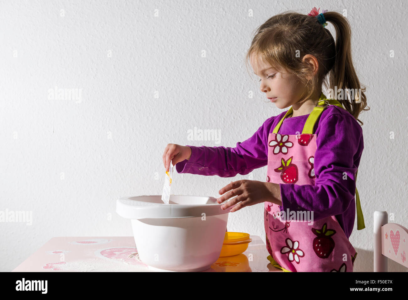 Una bionda bambina di tre anni è in cottura biscotti di Natale, versare gli ingredienti in un recipiente bianco Foto Stock