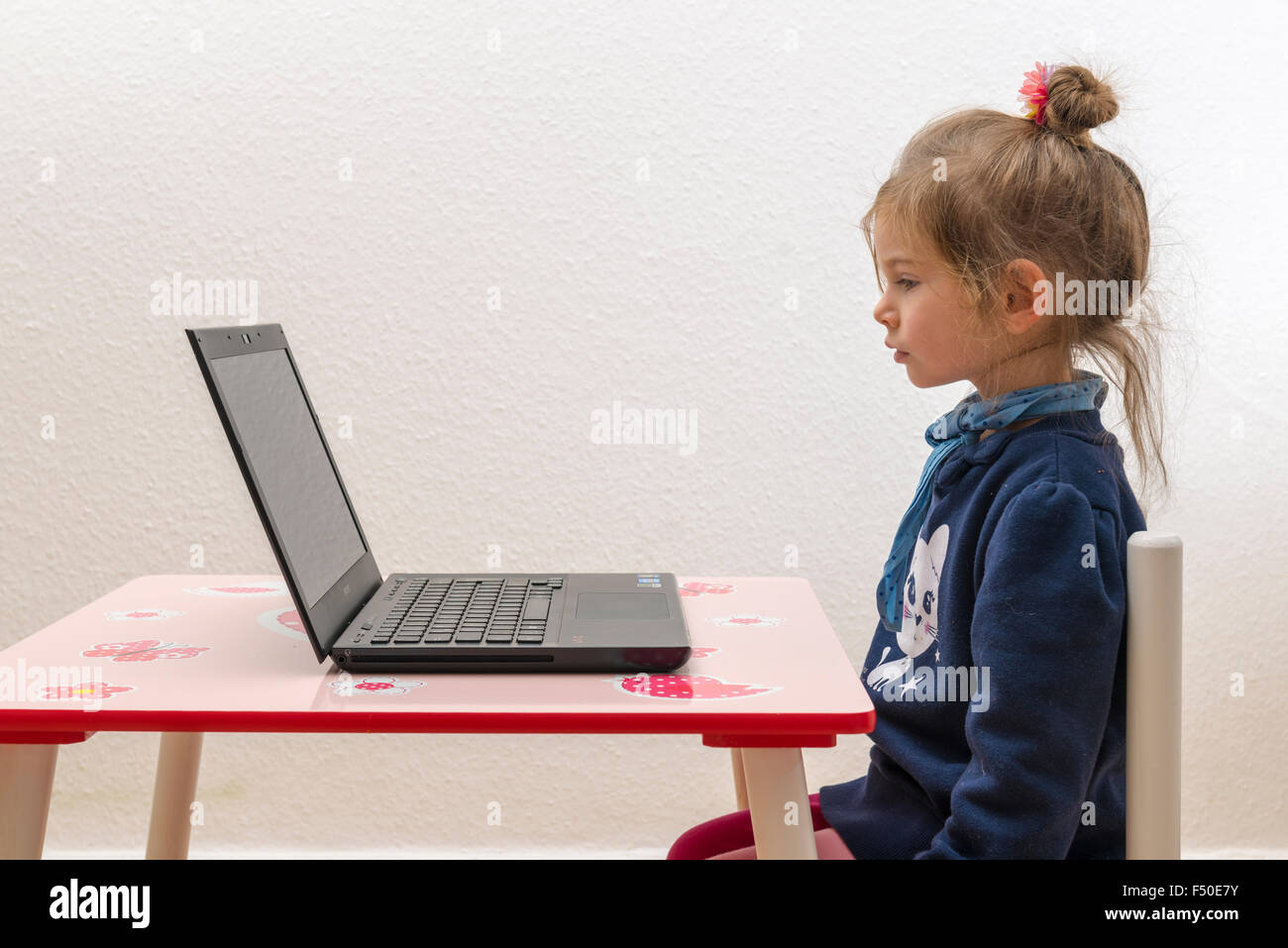 Una bionda bambina di tre anni è seduto davanti a un notebook, laptop, guardando lo schermo Foto Stock