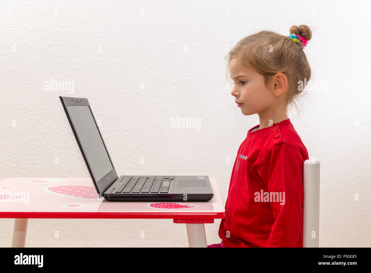 Una bionda bambina di tre anni è seduto davanti a un notebook, laptop, guardando lo schermo Foto Stock