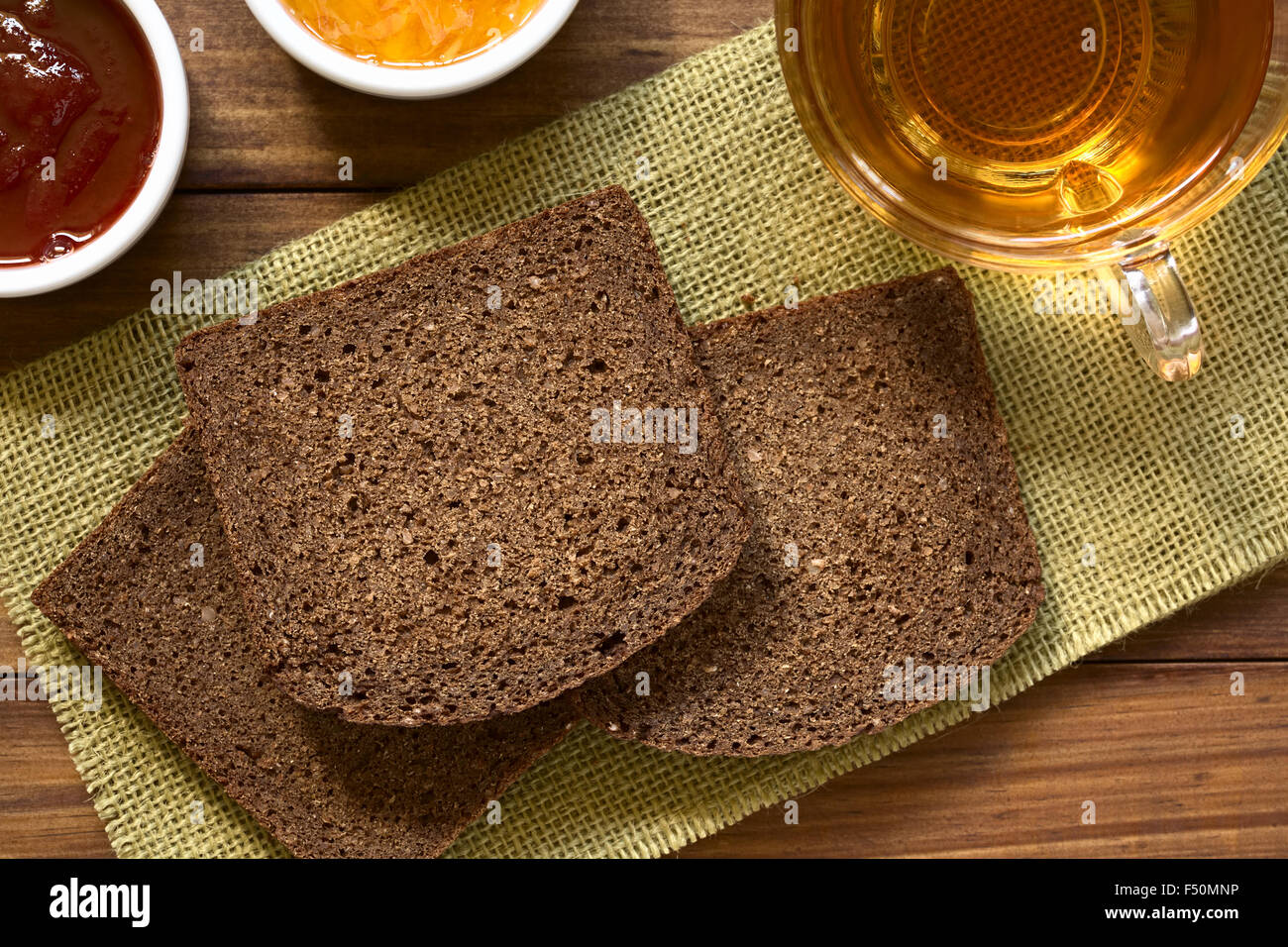 Fette di pumpernickel dark pane di segale con fragola e orange marmellata, tazza di tè sul lato Foto Stock