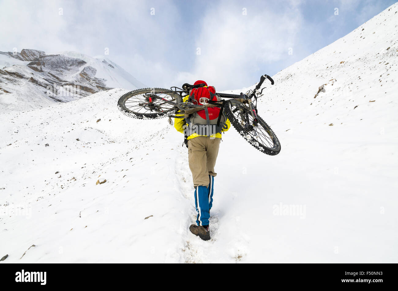 Ciclista portando la sua bici sulla neve fino verso thorong la pass Foto Stock