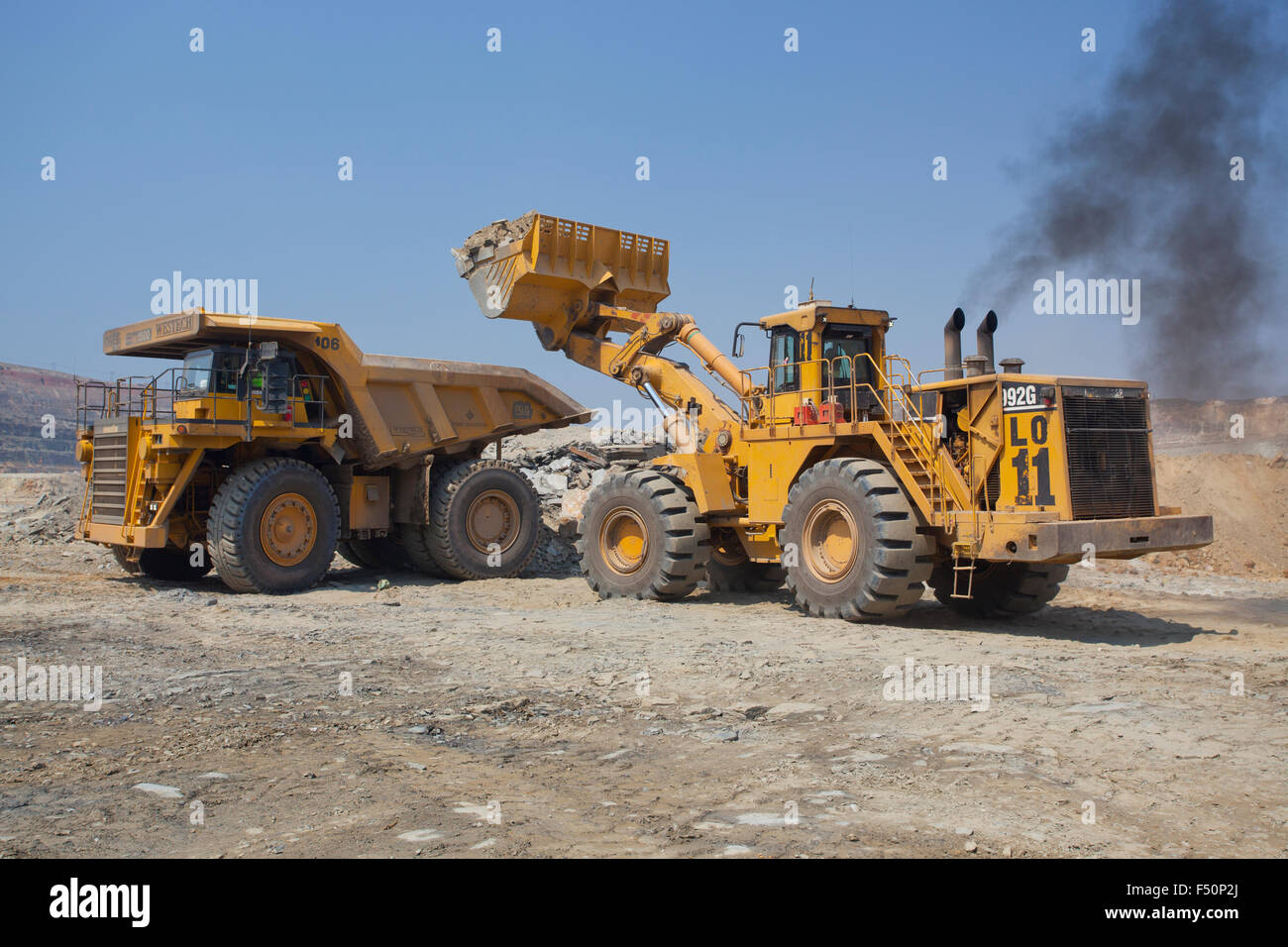 Azione girato di un caricatore a estremità anteriore il riempimento di una grande haul dump il mio carrello con terreno scavato. Settore minerario in Zambia, Africa. Foto Stock